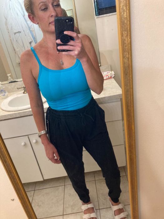 The reviewer is wearing black tie-waist joggers paired with a blue camisole top and white slide-on sandals.