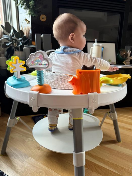 A baby seated in an activity center with various interactive toys, gazing off to the side