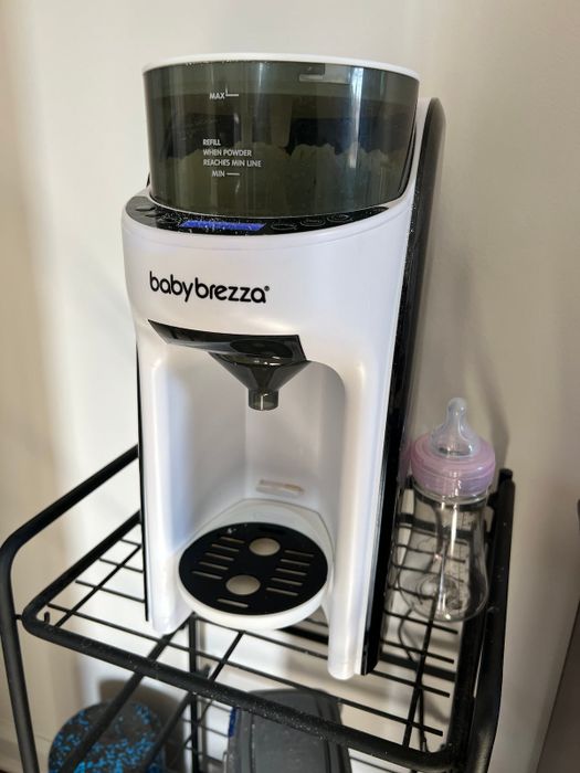 The Baby Brezza Formula Pro machine on a shelf with a baby bottle beside it, simplifying the formula-making process for parents