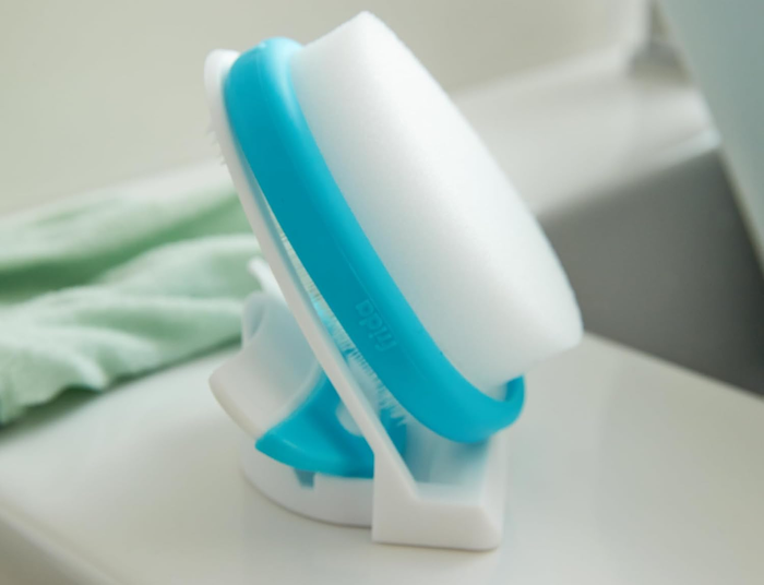 A sponge and its holder placed on the edge of a sink with text: