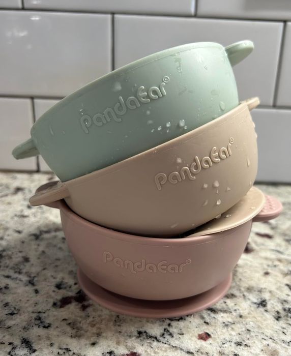 A stack of PandaEar silicone baby bowls on a granite countertop