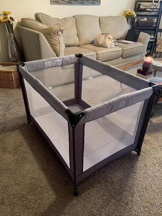 A baby playpen set up in a living room, surrounded by a couch, table, and decor