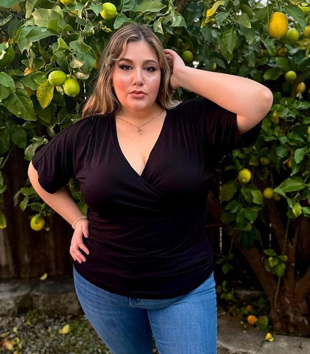 A reviewer posing with their hand in their hair in front of a lemon tree, wearing a black v-neck top and jeans