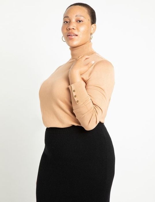 A model wearing a tan sweater tucked into a black skirt.