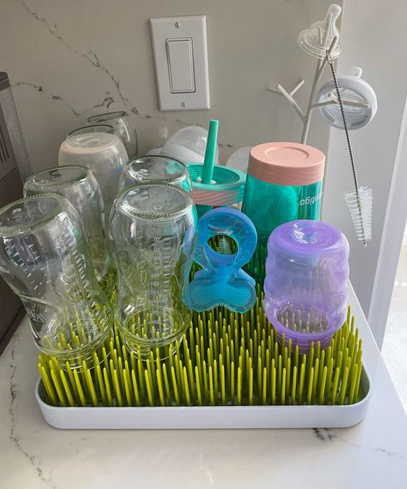Bottles, pacifiers, and sippy cups drying on a plastic grass-themed rack