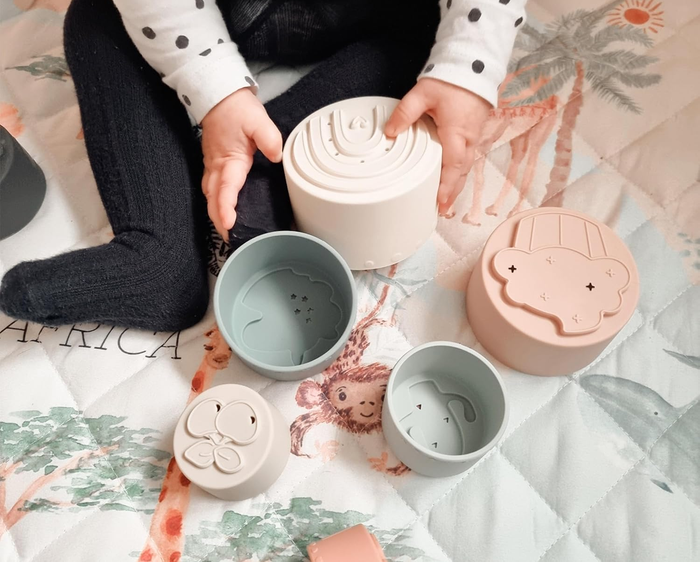 A baby plays with textured stacking cups on a quilt. Text highlights the engaging patterns designed to capture the infant's interest