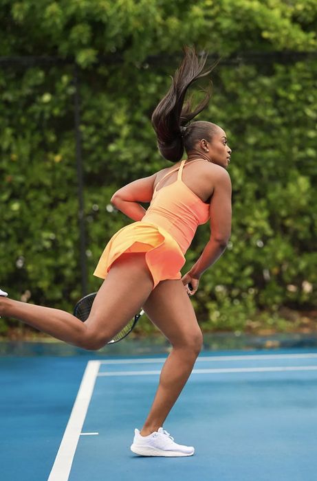 A model in an orange running romper caught mid-swing during a tennis match.