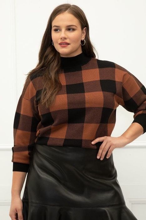 A model showcasing the plaid sweater paired with a leather skirt, viewed from the front.