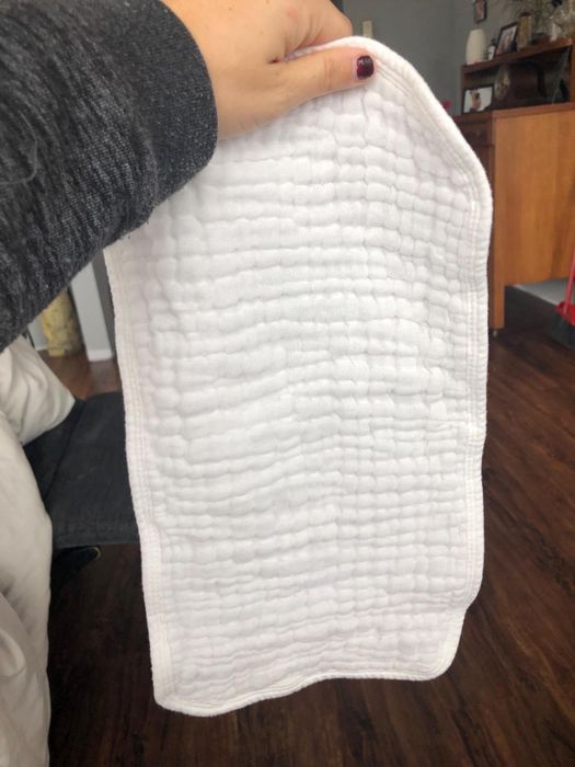 A hand holding a textured, white burp cloth in a cozy home setting