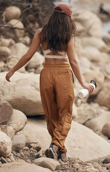 Another model hiking across rocky terrain in brown pants while holding a water bottle
