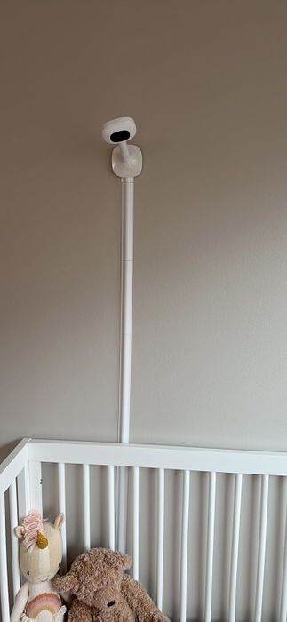 A baby monitor attached to the wall above a crib, with a stuffed unicorn and teddy bear on display. This setup is perfect for articles focused on nursery shopping.
