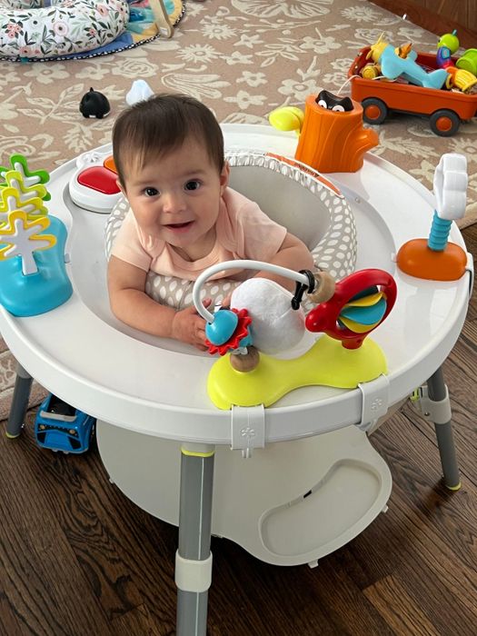 A baby enjoying playtime in an activity center, surrounded by colorful toys, with scattered play items on a wooden floor