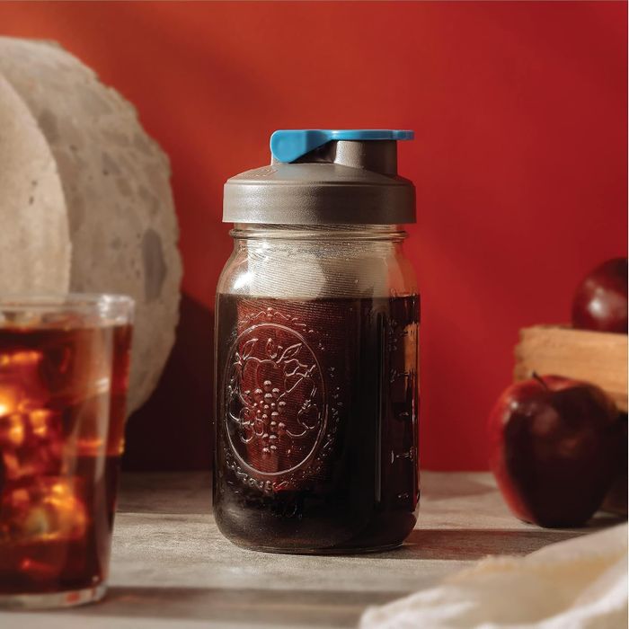 A mason jar with a lid, filled with iced coffee, accompanied by a glass of iced coffee and apples, showcasing kitchen essentials