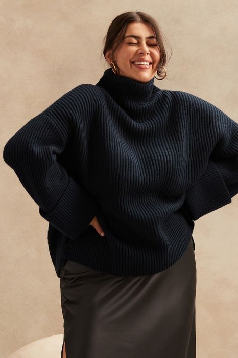 A model showcasing a black sweater paired with a black skirt.
