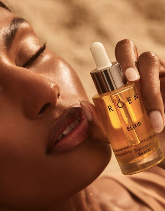 a model holding a golden bottle of restorative face oil