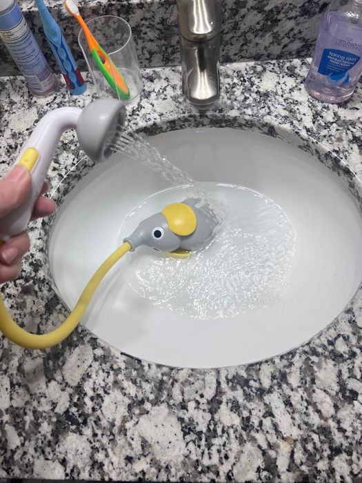 An elephant-themed faucet attachment spraying water into a bathroom sink, shown as part of a kid-friendly bath product setup