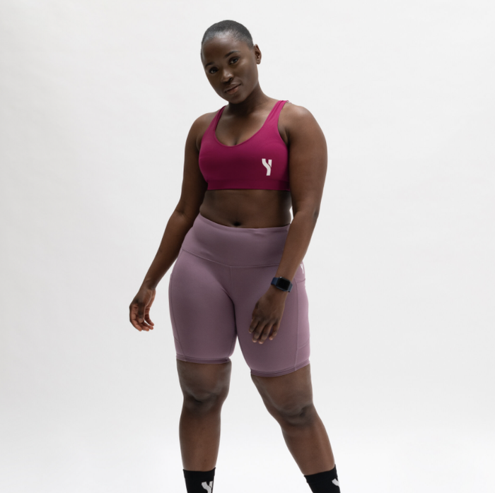 The model is wearing a vibrant hot pink sports bra and soft lavender shorts.