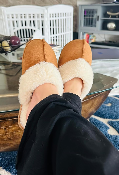 A person relaxes in cozy, fluffy slippers, with their feet comfortably propped on a table in a serene setting.