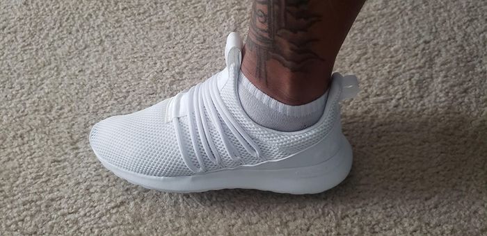 A reviewer demonstrates the laced white shoe, crafted from mesh fabric, with a convenient loop at the heel for easy wear.