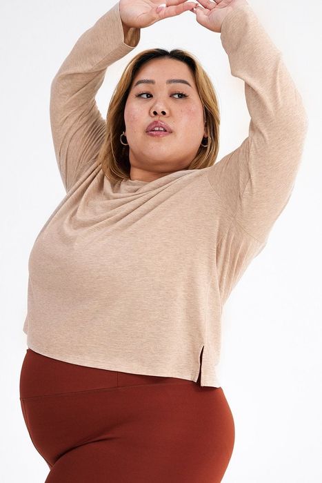 The model is sporting a sand-colored long-sleeve tee paired with clay-colored workout shorts.