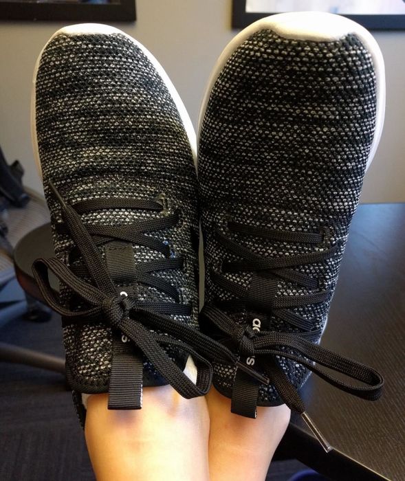 A reviewer crossing their feet while sporting the grey sneakers with laces.