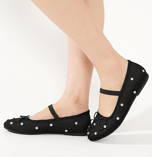 A person dons black ballet flats, stylishly adorned with tiny decorative gems, showcasing a chic and trendy look.