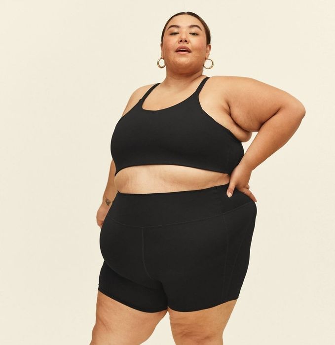 The model is sporting a black sports bra paired with matching black running shorts for a sleek, monochrome look.
