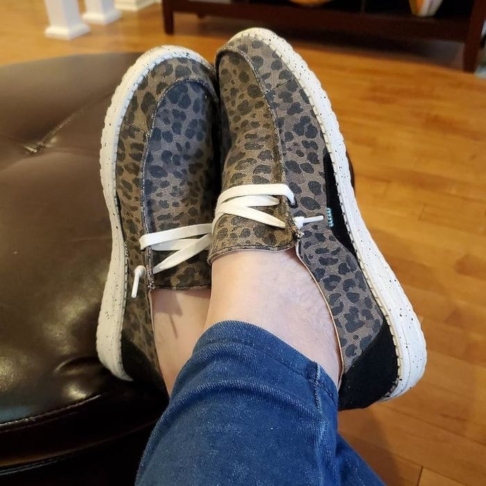 A reviewer is sporting slip-on shoes with white laces and a bold animal print design.