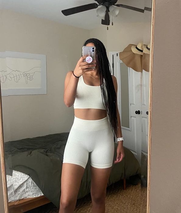 The reviewer is sporting a white ribbed workout set consisting of shorts and a tank top.