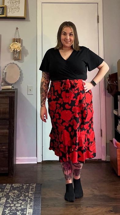 Person dressed in a black top and red floral skirt, posing with hands on hips