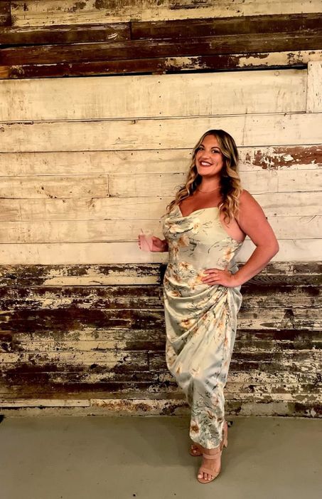 A reviewer in a floral dress poses in front of a rustic wooden background, highlighting the elegance of the design.