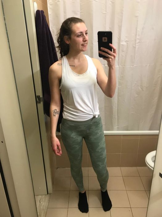 The reviewer is wearing a white tank top and green camouflage leggings.