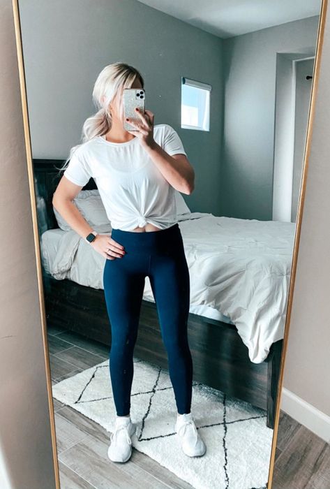 The reviewer is seen sporting a white T-shirt tied at the front, black leggings, and white sneakers.