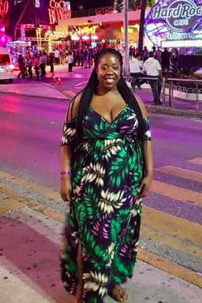 A reviewer showcasing a dress featuring a black, white, green, and purple leaf print.