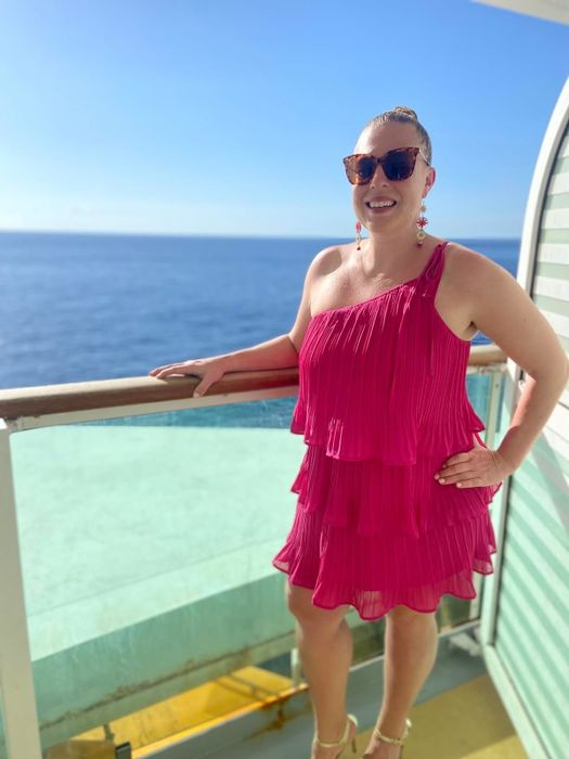 A person smiles on a ship's deck, wearing a tiered, sleeveless dress with the ocean as a backdrop