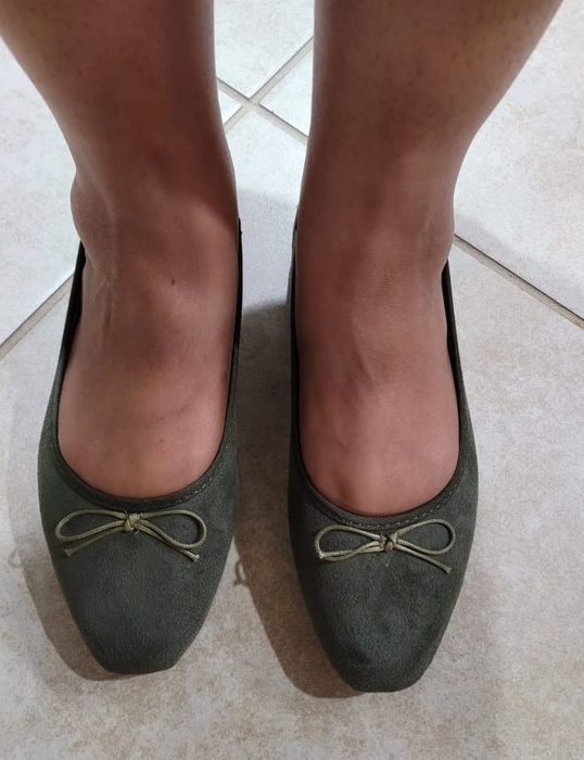 A close-up shot of a person's feet showcasing green ballet flats with bows adorning the toes, making for a stylish and playful look.