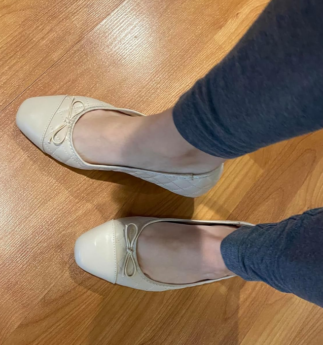 A person is trying on beige ballet flats with cute bow details, adding a charming touch to their outfit.