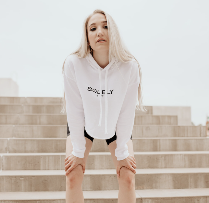 The model is wearing a white cropped hoodie paired with black shorts.