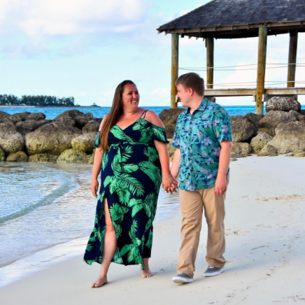 A reviewer strolling along the beach in a navy cold-shoulder dress adorned with green leaves.