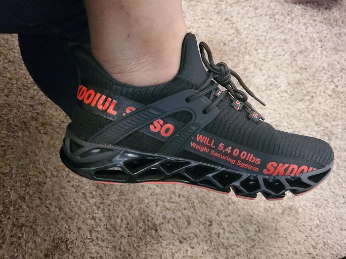 These black sneakers feature red lettering along the side, reinforced black accents, and a partially open bottom for enhanced breathability.