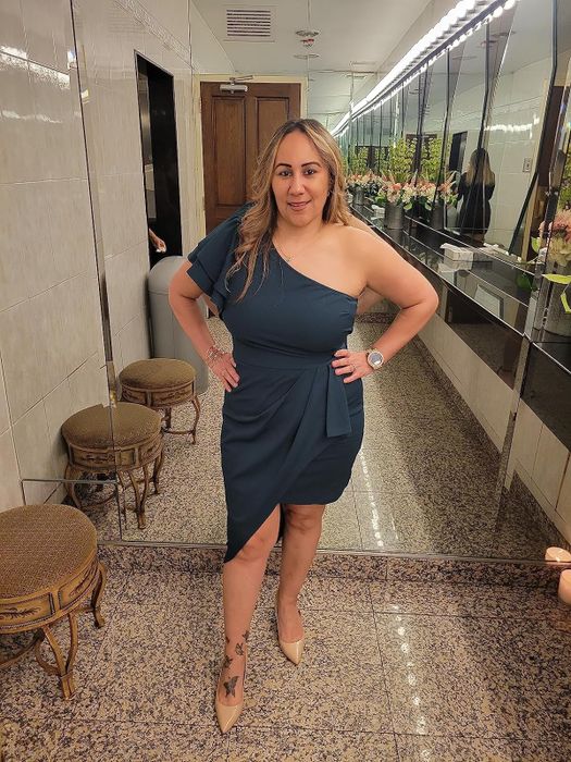 Woman in a stylish one-shoulder navy blue dress and nude heels, posing with a hand on her hip