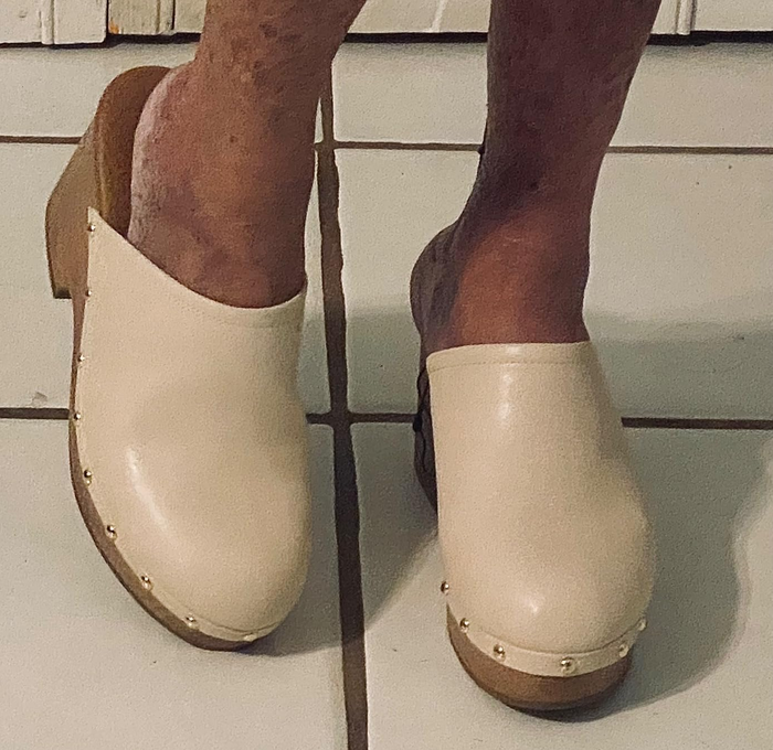 A person wearing trendy slip-on clogs with a wooden sole and studded embellishments.