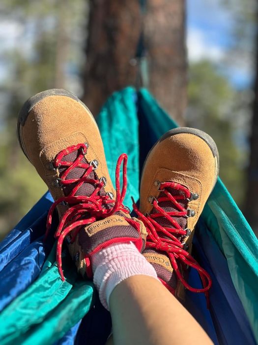 A person lounging in a hammock, wearing red-laced hiking boots and pink socks.