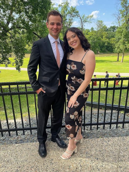 A couple dressed semi-formally: man in a black suit and woman in a floral dress, posing together outdoors