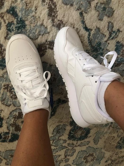 A reviewer shows off the white sneakers, featuring matching laces and a thick, supportive sole.