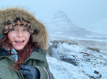 The writer in a snowy landscape with their naturally curly hair peeking out from under their winter hat