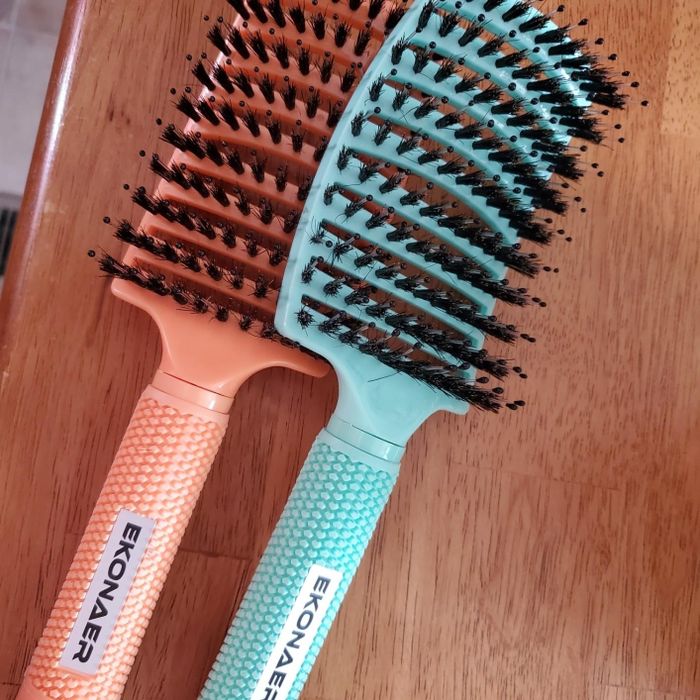 Two vented Ekonmer hair brushes with textured handles, resting on a wooden surface.