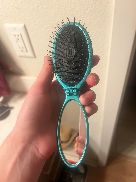 The reviewer's teal travel brush with a mirror on one side