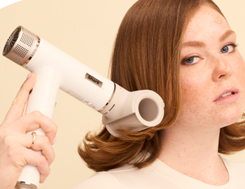 A person styling their hair using the blow dryer with a round attachment.
