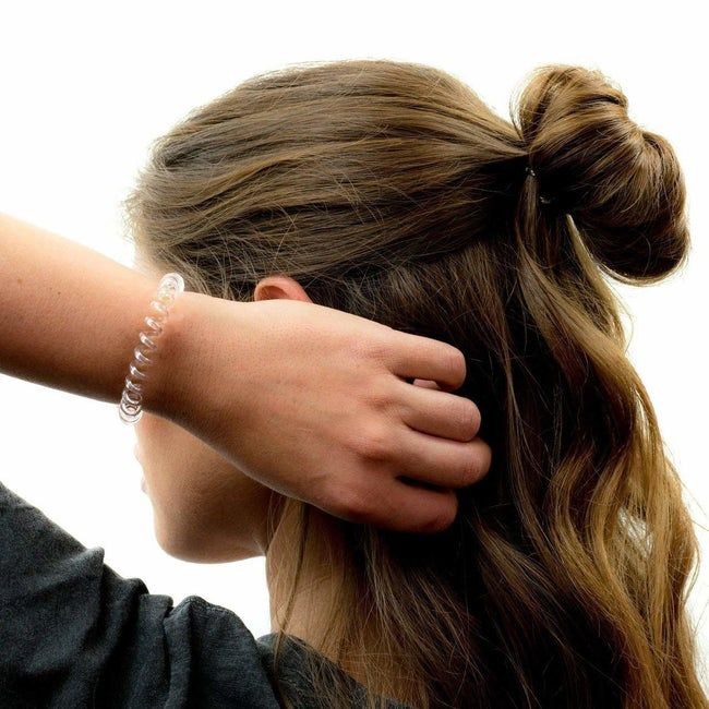 Model with the top section of their hair styled in a messy bun, wearing the phone cord-like spiral hair tie on their wrist.